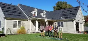 Five people stand on a lush lawn, with the sun setting behind a house equipped with solar panels, showcasing the growing trend of solar in Maine.